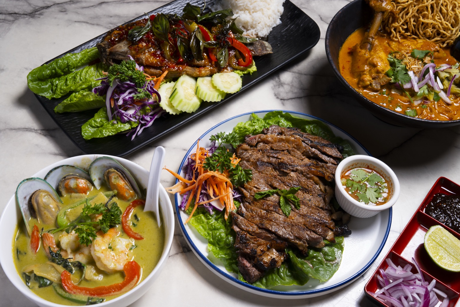 Top view of a traditional Thai meal with curry, rice, and spring rolls.